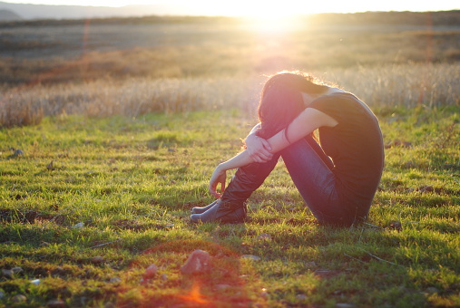 Profile view of woman sitting in grass with face in knees