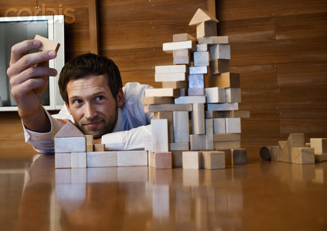 Young businessman constructing a building of blocks of wood --- Image by © Holger Scheibe/Corbis